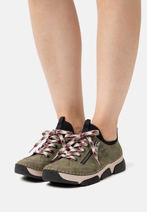 Baskets en suède vert avec accents noirs, dotées de semelles texturées, de lacets tissés colorés et d'un détail de fermeture éclair sur le côté.