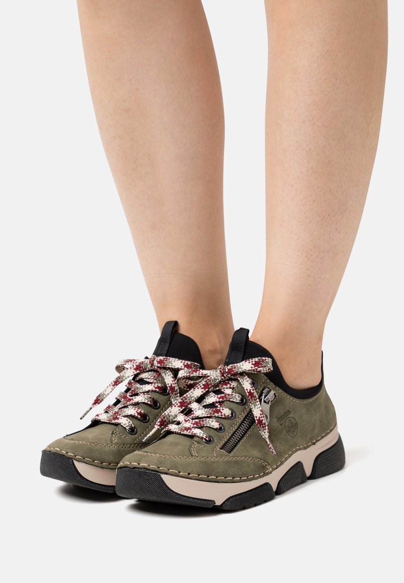 Baskets en suède vert avec accents noirs, dotées de semelles texturées, de lacets tissés colorés et d'un détail de fermeture éclair sur le côté.