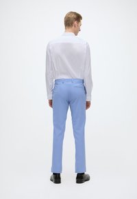 Calças azul claro com um ajuste slim, combinadas com uma camisa branca de colarinho. Textura suave, design minimalista e sapatos pretos.