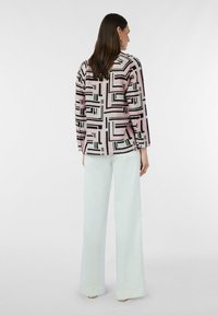 Różowa koszula z długim rękawem z czarnymi geometrycznymi wzorami, zestawiona z jasnoniebieskimi spodniami typu wide-leg. Gładki materiał o luźnym kroju.