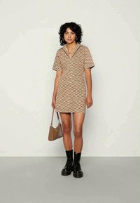 Vestido castanho com um padrão em zigzag, mangas curtas e decote em V. Combinado com botins pretos e uma mala castanha.