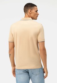 Beige poloshirt van katoen, met een puntige kraag en korte mouwen met een blauwe accent op de boorden. De achteraanzicht toont een gladde textuur.