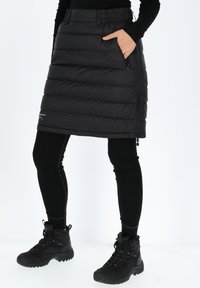 Svart isolerad kjol med puffy design, med sidofickor och mudd i midjan, tillsammans med svarta leggings och vandringskängor.