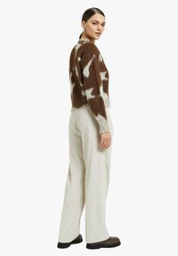 Maglione lavorato a maglia con motivo marrone e bianco con polsini a coste, abbinato a pantaloni larghi color crema a coste e scarpe nere. Vista laterale dell'outfit.