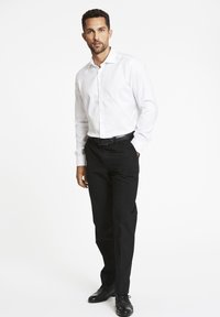 Witte lange mouwen overhemd, zwarte broek en zwarte schoenen. Het overhemd heeft een kraag en knopen, terwijl de broek een rechte pasvorm heeft.