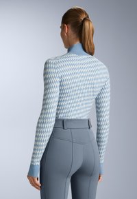 Ljusblå, figurnära tröja med ett texturerat diamantmönster, kombinerad med högmidjade grå byxor med en tjock midjeband och sömdetaljer.