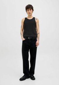 Débardeur noir côtelé associé à un jean noir taille haute. Les accessoires comprennent une ceinture noire et des chaussures noires, le tout sur un fond neutre.