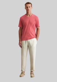 T-shirt rouge à manches courtes et encolure en V associé à un pantalon en lin crème et des chaussures bateau beiges. Design simple, tissu léger, coupe décontractée.