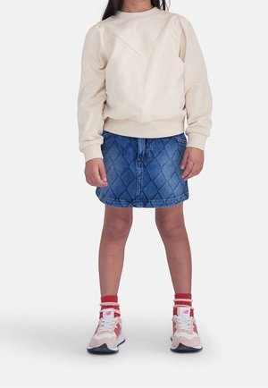 Beiger Pullover mit einem mit Rautensteppung versehenen Jeansrock. Pink-rote Turnschuhe mit weißen Akzenten. Weicher Stoff und lässiges Design.