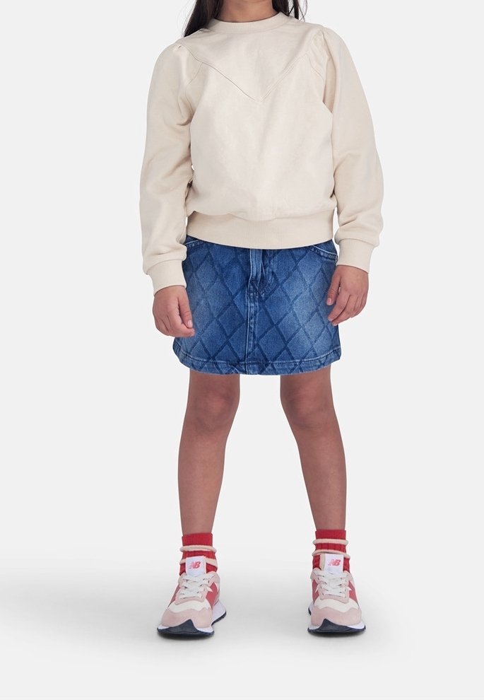 Sweat-shirt beige avec une jupe en denim matelassée en forme de losange. Baskets roses et rouges avec des accents blancs. Tissu doux et design décontracté.