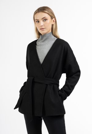 Black wrap-style coat made of soft fabric, featuring a belted waist, loose sleeves, and side pockets, layered over a gray turtleneck.