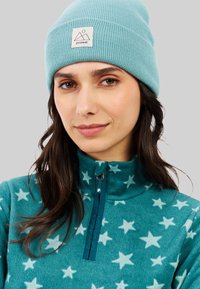 Pullover in fleece turchese con motivi a stella bianchi, dotato di collo con zip e un accento verde acqua, abbinato a un berretto a coste blu chiaro.