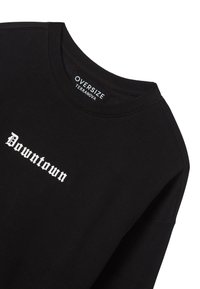 Felpa nera oversize realizzata in misto cotone, con testo bianco "Downtown" in un carattere audace. Collo a girocollo con costine e tessuto testurizzato.
