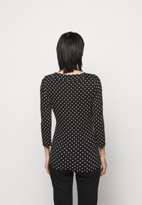 Mustaan pitkähihaisen puseron, jossa on valkoisia pilkkuja, muotoiltu malli, pyöreä kaula-aukko ja puolihipulle ulottuva pituus, paritettu mustien housujen kanssa.