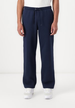 Tmavomodré tepláky z mäkkej látky, s elastickým pásom so šnúrkou a bočnými vreckami, zužujúce sa pri členkoch.