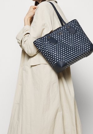 Marineblauwe tote bag met polkadots en leren accenten, met dubbele handgrepen en een gestructureerde vorm. Heeft een merklogo aan de voorkant.