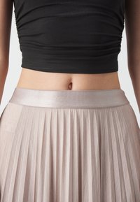 Gros plan du milieu du corps d'une personne portant un haut court noir et une jupe plissée taille haute rose clair.