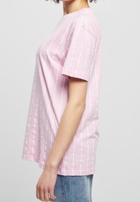 Růžové pruhované tričko s krátkým rukávem a volným střihem, zdobené bílými svislými pruhy na měkké, lehké látce.