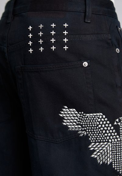 Jeans de denim negro con adornos metálicos de cruces en el bolsillo trasero y un patrón texturizado en el lateral, con detalles en plata.