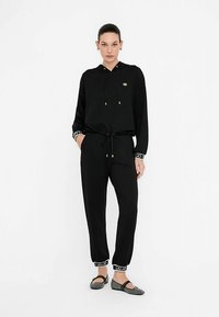 Schwarzes Hoodie- und Jogginghose-Set aus weichem Stoff, mit Kordelzug, goldenen Akzenten und kontrastierenden gemusterten Bündchen mit Logodetails.