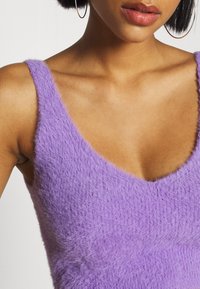 Top sin mangas morado de peluche con un escote en V profundo y tirantes anchos, que presenta una textura suave y una forma ajustada.