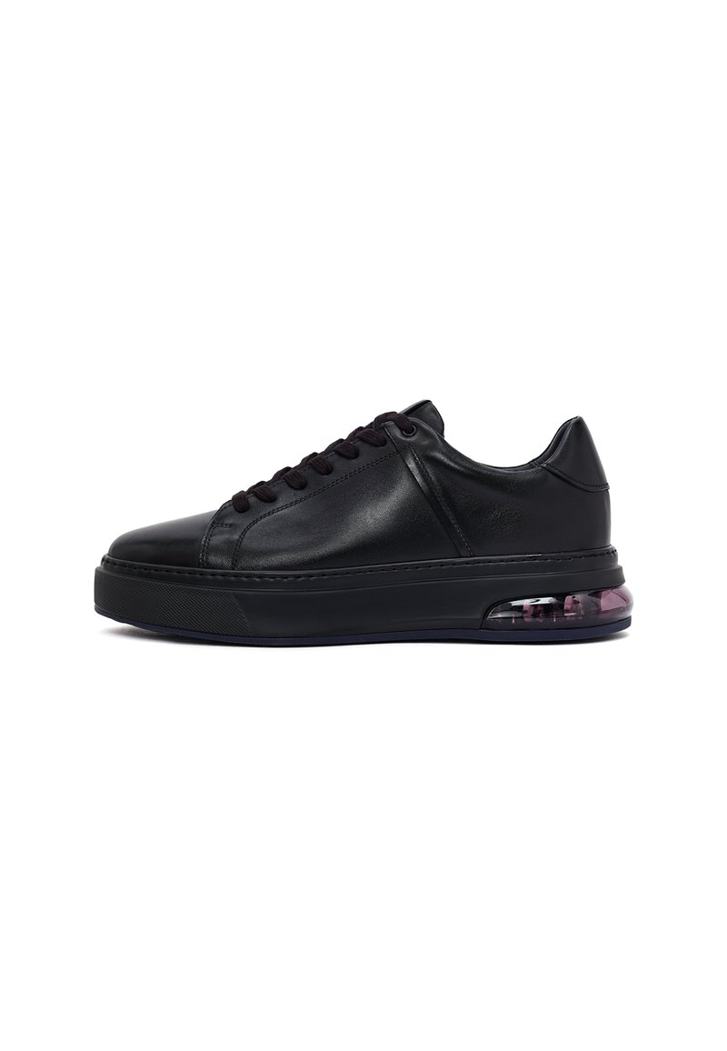Zapatilla baja de cuero negro con suela gruesa y unidad de amortiguación visible en el talón, que presenta cordones negros y detalles de costura.