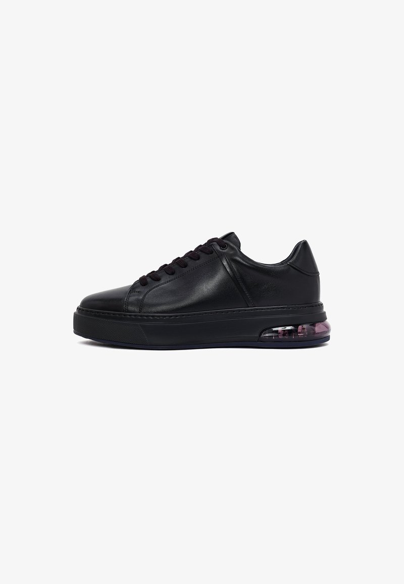 Black leather low-top sneaker with thick sole and visible air cushion unit in the heel, featuring black laces and stitching details.