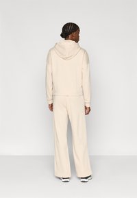 Kreminio spalvos trumpa palaidinė su kišene nugarinėje pusėje, derinama su plačiomis kelnėmis. Lygus, minkštas audinys su subtilia tekstūra.