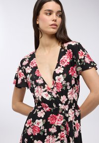 Abito floreale nero con maniche corte a volant, scollatura a V profonda e vita elastica. Presenta motivi di fiori rosa e bianchi in tutto l'abito.