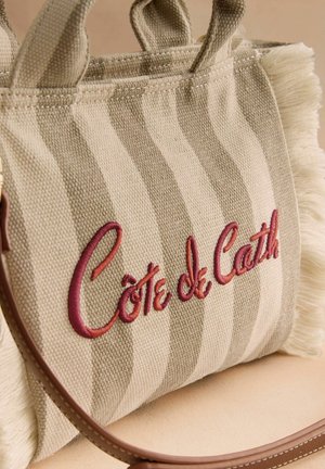 Beżowo-kremowa paskowana torba materiałowa z frędzlami na brzegach i czerwonym haftem "Côte de Cath" po boku.