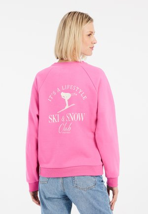 Roze sweatshirt met een ronde hals, raglanmouwen en witte bedrukte tekst op de achterkant met een skiër grafiek en clubbranding.