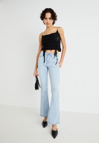 Svart crop topp med teksturert stoff, justerbare bånd og sølvstropper. Lyseblå, utsvingte jeans som sitter godt over hoftene, med en avslappet silhuett.