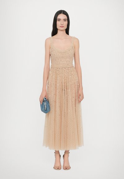 Abito in tulle beige con design a strati, adornato da paillettes e con un corpetto aderente. Abbinato a una pochette blu con texture e tacchi nudi.