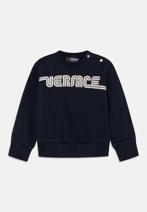 Granatowy sweter z długim rękawem z kremowym logo Versace na klatce piersiowej i dwoma złotymi guzikami na lewym ramieniu.