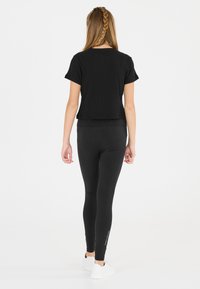 Mustat lyhythihaiset cropped-t-paidat yhdistettynä mustiin legginsseihin. Molemmissa vaatteissa on sileä pinta ja ne on valmistettu venyvästä kankaasta.