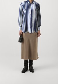 Striped blue and white button-up shirt, beige satin skirt, and black ankle boots; holding a small black handbag. Smooth textures, casual design.