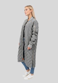 Gevoerde grijze lange jas met zijrits zakken, geribde manchetten en een ritssluiting aan de voorkant. Draag met een zwarte top en blauwe jeans met witte sneakers.