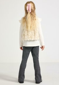 Faux fur vest i creme, langærmet hvid top, teksturerede mørkegrå flagrende bukser, med pink hårsløjfer i langt, bølget hår.