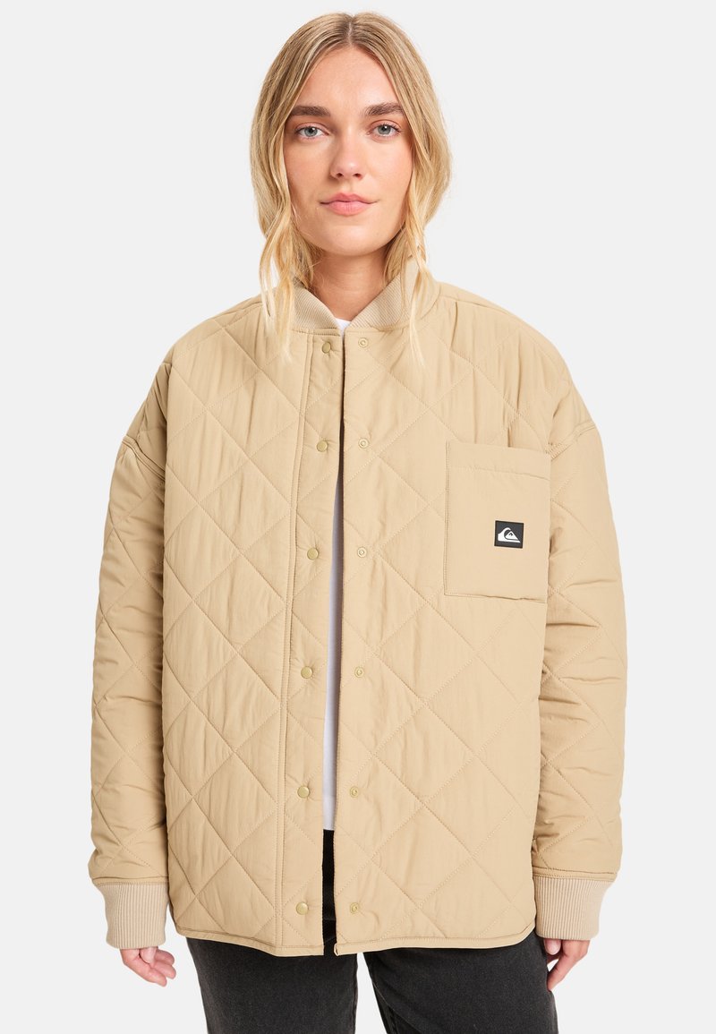 Beige quiltet jakke med knappelukking, ribbede mansjetter og brystlomme med et merket logo. Glatt tekstur med en rett passform.