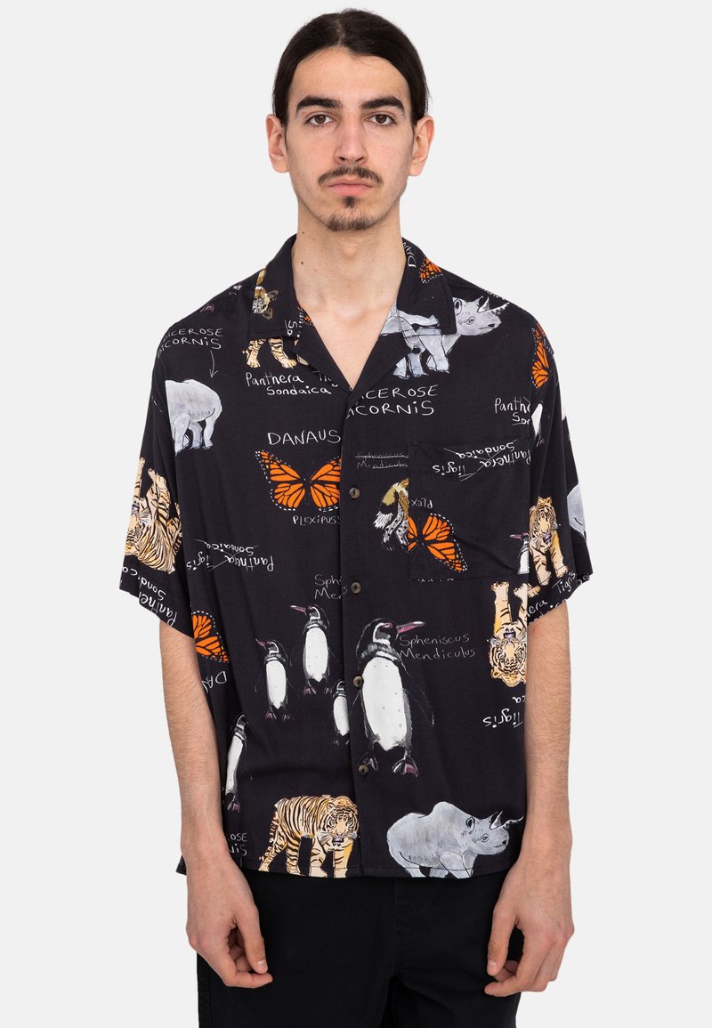 Camisa de manga corta negra con ilustraciones de animales (tigres, pingüinos, mariposas) con texto blanco y acentos coloridos, hecha de tela ligera.