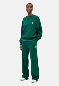 Sweatshirt vert et pantalon assorti en tissu doux. Le sweatshirt arbore un petit logo blanc ; le pantalon a une taille rayée et des poches latérales.