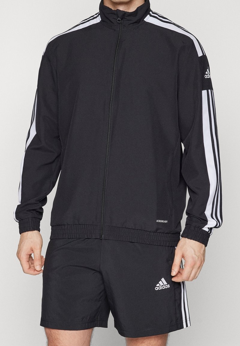 Black athletic jacket with white stripes, zip front, high collar, and fitted cuffs. Paired with matching black shorts and Adidas logo accents.