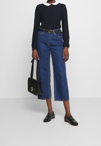 Marinblå stickad långärmad topp med vit krage, i kombination med avklippta blå denimjeans. En svart handväska och loafers fulländar outfiten.