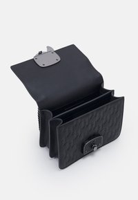 Musta nahkainen olkalaukku, jossa on jämäkkä muoto, kuvioituna kohokuvioidulla houndstooth-kuosilla, metallinen lukko ja useita sisäosia.