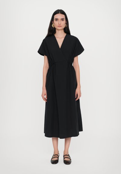 Robe noire à manches courtes, taille cintrée et jupe fluide. Le matériau semble lisse avec des coutures minimales visibles.
