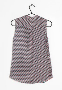 Ärmellose Bluse mit geometrischem Muster, die rote, blaue und türkisfarbene Formen auf weißem Hintergrund zeigt; abgerundeter Saum und Faltendetail.