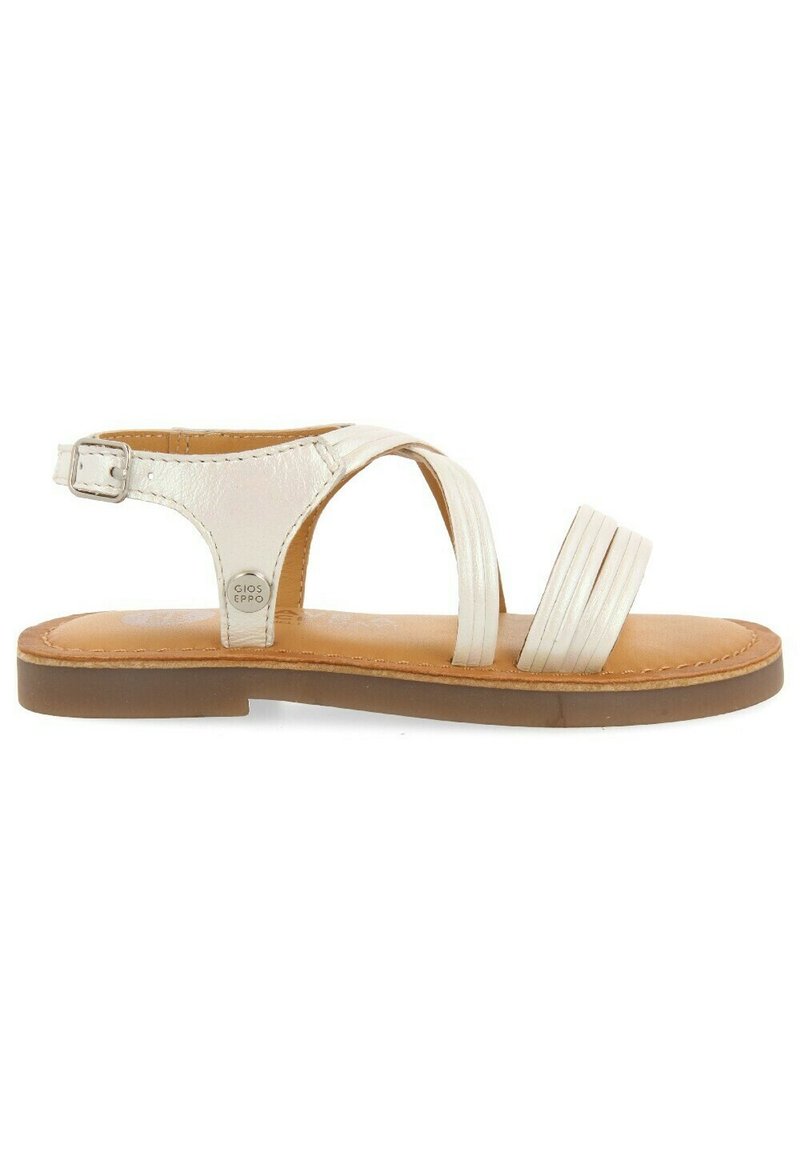 Sandal in pelle bianca con cinturini incrociati, fibbia alla caviglia regolabile e suola piatta marrone. Presenta design di cinturini testurizzati e lisci.