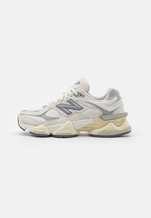 Vita och grå New Balance-sneakers med mesh- och mockamaterial, en kraftig sula och texturerade detaljer på sidorna och hälen.