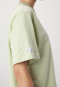 Světle zelené bavlněné tričko, krátké rukávy, s jemným logem Nike na bílé nášivce na rukávu, má pohodlný střih a měkkou texturu.