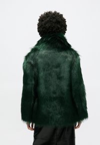 Πράσινο παλτό από ψεύτικη γούνα με ψηλό γιακά, υφή στην επιφάνεια και χαλαρή σιλουέτα. Ολοκληρώνεται με μακριά μανίκια και cropped μήκος.